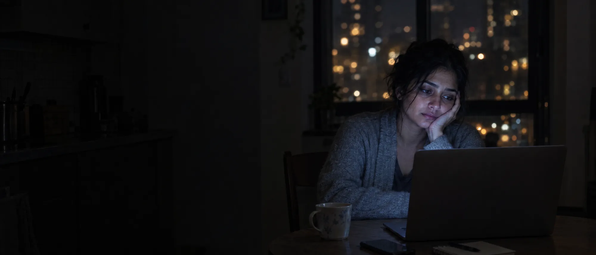 A woman at her kitchen table late at night, laptop glow